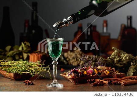 Green herbal liquor is poured from a vintage bottle into a glass. 110334436