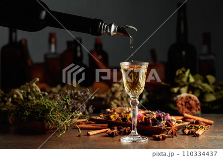 Yellow herbal liquor or mixture is poured from a vintage bottle into a glass. 110334437