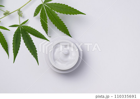 Container of hemp cream top view on white background. Cannabis body cream or face cream with marijuana leaf. Container of hemp cream top view on white background. Cannabis body cream or face cream with marijuana leaf. 110335691
