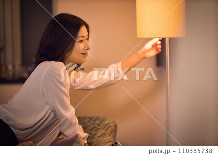 ジャケットを脱いでスタンドの電気をつけるビジネスウーマンのナイトルーティーン ジャケットを脱いでスタンドの電気をつけるビジネスウーマンのナイトルーティーン 110335738