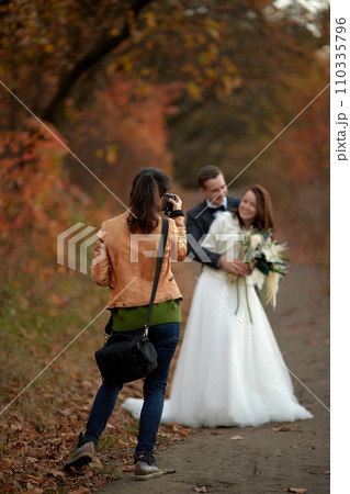 female wedding photographer taking pictures of the bride and groom on the wedding day in autumn female wedding photographer taking pictures of the bride and groom on the wedding day in autumn 110335796