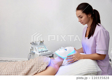 woman getting cosmetic procedure with LED facial mask in beauty salon 110335828