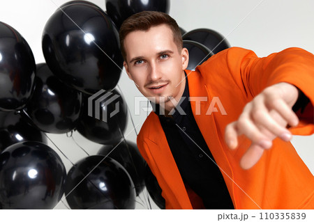 handsome man in orange jacket with black air balloons on white background. birthday party handsome man in orange jacket with black air balloons on white background. birthday party 110335839
