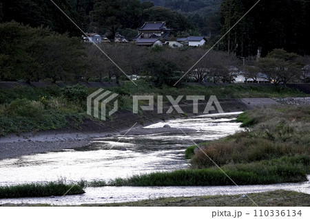 夕暮れ時の河川と高台に建つ日本建築の民家 110336134
