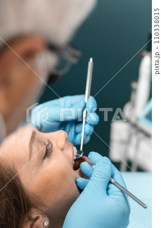 A patient sits in a dental chair with a smile, expressing her impression of refreshment and lightness after a visit to the dentist. The doctor, holding instruments in his hands, is ready for further 110338015