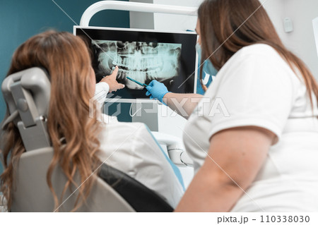 The dentist shows the patient a panoramic X-ray on the monitor, carefully explaining all the details and features of her dental condition. A dentist with great professionalism shows the patient a The dentist shows the patient a panoramic X-ray on the monitor, carefully explaining all the details and features of her dental condition. A dentist with great professionalism shows the patient a 110338030