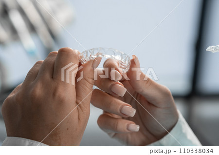 The dentist carefully holds the mouth guard in his hands, preparing for the procedure and demonstrating his adaptability to the highest standards of dental practice. 110338034