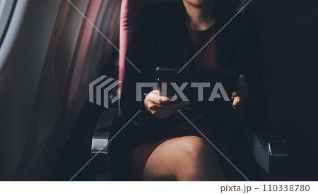 Blonde female tourist checking incoming notification on smartphone sitting on seat of airplane with netbook.Young businesswoman share media from telephone on laptop computer during plane flight 110338780