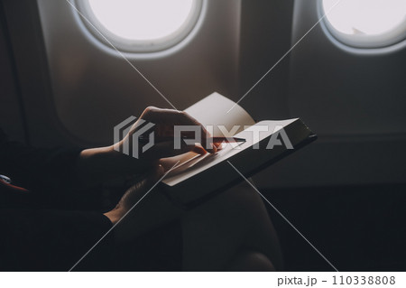 Blonde female tourist checking incoming notification on smartphone sitting on seat of airplane with netbook.Young businesswoman share media from telephone on laptop computer during plane flight 110338808
