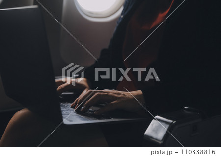 Blonde female tourist checking incoming notification on smartphone sitting on seat of airplane with netbook.Young businesswoman share media from telephone on laptop computer during plane flight 110338816