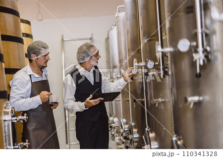 Winemaker professional working in modern large winery factory liquor alcohol drinks industry quality control and fermentation monitor vintage color tone Winemaker professional working in modern large winery factory liquor alcohol drinks industry quality control and fermentation monitor vintage color tone 110341328