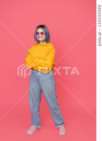 Smiling Asian teenager in crossed hands position with colored hair stylishly dressed in yellow jacket, standing on pink background. Youth culture, girl's expressive style and personality in 110342080