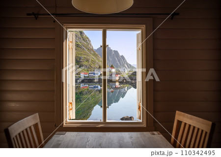 View through a Rorbu window captures Lofoten's mountains and charming Norwegian homes 110342495