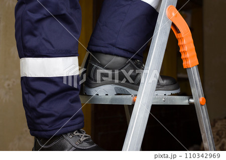 Legs of builder in special warm clothes and boots climb up metal stepladder. Concept of repair at height 110342969
