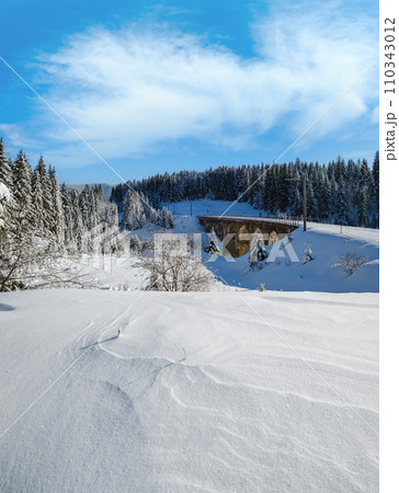 Stone viaduct (arch bridge) on railway through mountain snowy fir forest. Snow drifts  on wayside and hoarfrost on trees and electric line wires. 110343012