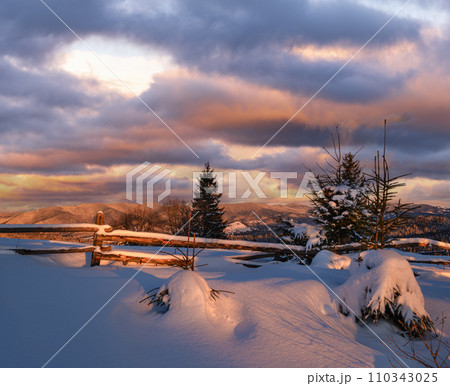 Alpine village outskirts in last evening sunset sun light. Winter snowy hills and fir trees. Alpine village outskirts in last evening sunset sun light. Winter snowy hills and fir trees. 110343025