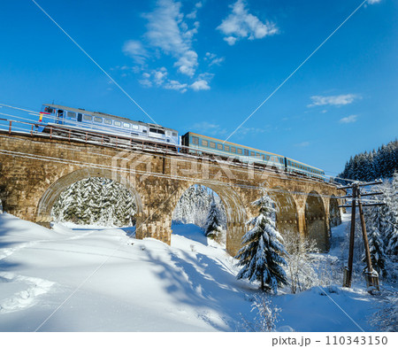 Stone viaduct (arch bridge) on railway through mountain snowy fir forest. Snow drifts  on wayside and hoarfrost on trees and electric line wires. 110343150