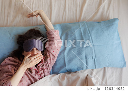 happy woman in bed wakes up, person in sleep mask stretches and yawns and enjoys her morning happy woman in bed wakes up, person in sleep mask stretches and yawns and enjoys her morning 110344022