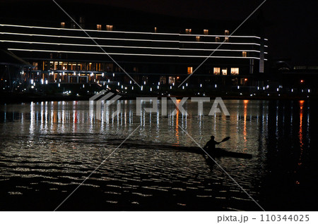 A Man Rowing a Kayak on the River in a City at Night. 110344025