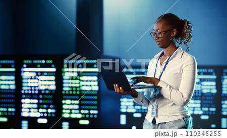 Computer scientist programming in server farm housing advanced equipment storing massive datasets. Developer running code on laptop to fix data center racks doing complex computational operations 110345255