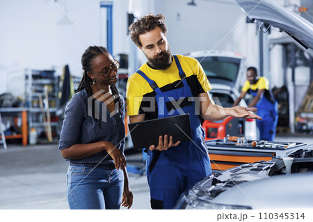 Mechanic at auto repair shop conducts annual vehicle checkup, informing customer about needed radiator replacement. Knowledgeable garage worker talks with customer after finishing car inspection Mechanic at auto repair shop conducts annual vehicle checkup, informing customer about needed radiator replacement. Knowledgeable garage worker talks with customer after finishing car inspection 110345314