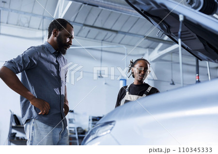 Mechanic at auto repair shop conducts annual vehicle checkup, informing customer about needed steering mechanism replacement. Competent garage worker talks with customer after finishing car inspection 110345333