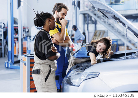 Team of mechanics in auto repair shop working together on fixing car, discussing best options. Multiethnic employees collaborating on servicing broken vehicle, checking for fuel tank Team of mechanics in auto repair shop working together on fixing car, discussing best options. Multiethnic employees collaborating on servicing broken vehicle, checking for fuel tank 110345339