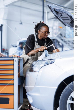 Engineer in car service use torque wrench to tighten bolts after replacing engine. African american skilled auto repair shop employee uses professional tools to fix customer automobile Engineer in car service use torque wrench to tighten bolts after replacing engine. African american skilled auto repair shop employee uses professional tools to fix customer automobile 110345340