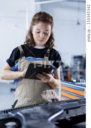 Diligent serviceman in car service orders new engine for damaged vehicle using tablet. Expert looking online for components to replace old ones in malfunctioning automobile 110345342