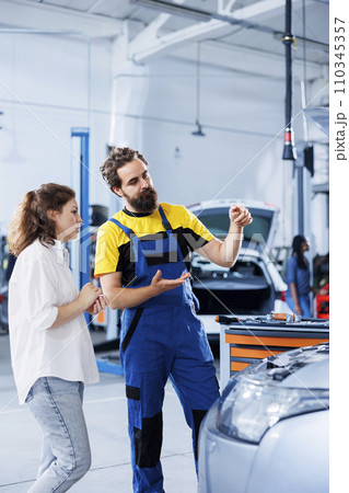 Adept repairman in repair shop using holographic AR technology to show customer car performance parameters. Garage worker using futuristic vr headset to inform client of issues found in vehicle Adept repairman in repair shop using holographic AR technology to show customer car performance parameters. Garage worker using futuristic vr headset to inform client of issues found in vehicle 110345357
