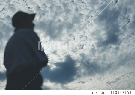 つなぎを半分脱いだ若い男性と青空 110347151