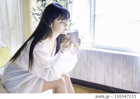 日差しがさしこむ部屋でコーヒーを飲む若い女性 110347215