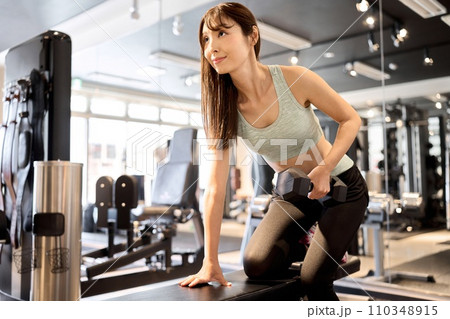 ワンハンドダンベルロウで背中と腕を鍛える女性 110348915