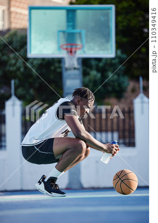 Basketball, sport and fitness with a young man on a court for exercise, training and workout. Health, wellness and fitness with a sporty person resting and drinking water after sports practice 110349416