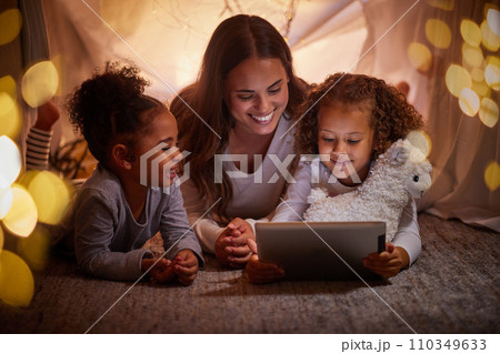 Mother and children live streaming on an app using a tablet in a tent camping at home at night. Happy mom and kids watching online content or playing games with house wifi in the dark or evening Mother and children live streaming on an app using a tablet in a tent camping at home at night. Happy mom and kids watching online content or playing games with house wifi in the dark or evening 110349633