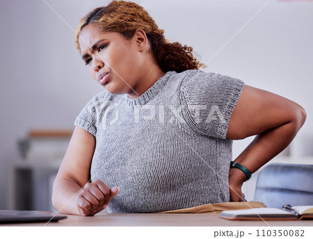 Corporate employee suffering from back pain while working at a desk in an office, uncomfortable and concerned. Young professional experience discomfort from an injury, bad posture or hurt muscle 110350082