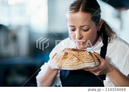 Baker, pastry chef and cafe owner smelling a loaf of fresh baked bread in the kitchen of her coffee shop. Closeup of a female cook enjoying the aroma of a freshly made dough treat or consumables 110350089