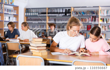 Two female friends reading books together and preparing for exams in school library Two female friends reading books together and preparing for exams in school library 110350887