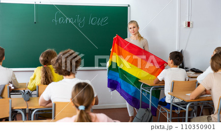 Progressive female teacher discussing with teenage students about LGBT social movements in classroom, holding rainbow flag Progressive female teacher discussing with teenage students about LGBT social movements in classroom, holding rainbow flag 110350901