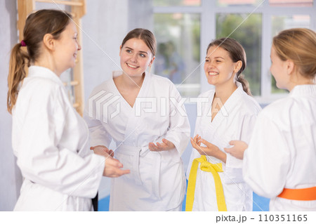 Teenage girls talking to coach and each other after karate training in gym Teenage girls talking to coach and each other after karate training in gym 110351165