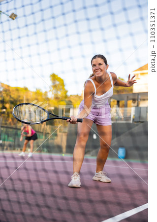 Positive girl in sportswear playing tennis match during training. View through tennis net 110351371