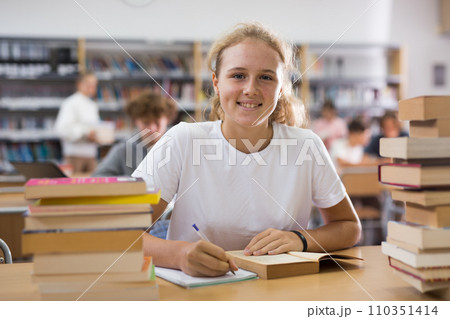 Portrait of teenager girl reading books and writing in notebooks in library 110351414