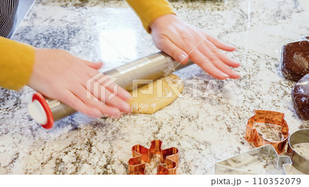 Using an adjustable rolling pin to roll out gingerbread cookie dough on the elegant marble counter in a modern kitchen, getting ready for festive holiday baking. Using an adjustable rolling pin to roll out gingerbread cookie dough on the elegant marble counter in a modern kitchen, getting ready for festive holiday baking. 110352079