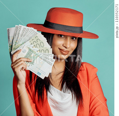 Rich, successful and wealthy young woman holding cash money after winning competition, lottery or casino prize. Smiling, elegant and trendy female with pay reward against a blue studio background 110352171