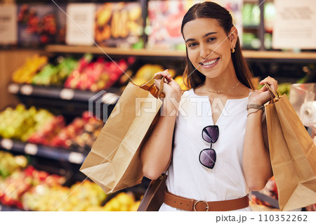 Grocery shopping, food and diet with a young woman in a retail, convenience store or grocer and fruit and vegetables in the background. Portrait of a female with paper bags in a fresh produce aisle Grocery shopping, food and diet with a young woman in a retail, convenience store or grocer and fruit and vegetables in the background. Portrait of a female with paper bags in a fresh produce aisle 110352262