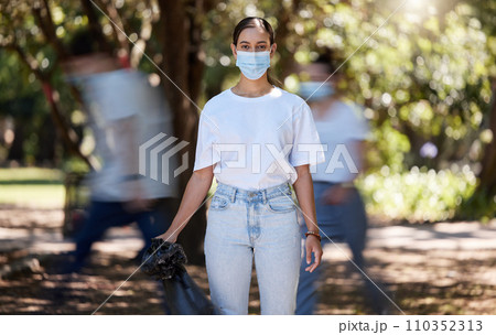Woman in covid face mask cleaning the park for clean, hygiene and safe green environment. Responsible activist, volunteer or community service worker with rubbish, trash and garbage in a plastic bag 110352313