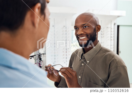 Shopping for glasses at an optician retail store with a smiling man trying to search for a pair. Optometrist and customer service employee selling a happy buying client new and modern spectacles 110352616
