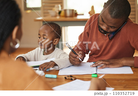 Busy and multitasking father talking on a call while taking care of his child at home. African american entrepreneur or freelancer analyzing paperwork with his wife caring for his busy little son Busy and multitasking father talking on a call while taking care of his child at home. African american entrepreneur or freelancer analyzing paperwork with his wife caring for his busy little son 110352719