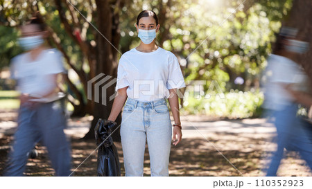 Female wearing covid mask cleaning the park for a clean, hygiene and safe green outdoor environment. Community service, volunteers or activist workers with rubbish, trash and garbage in a plastic bag 110352923