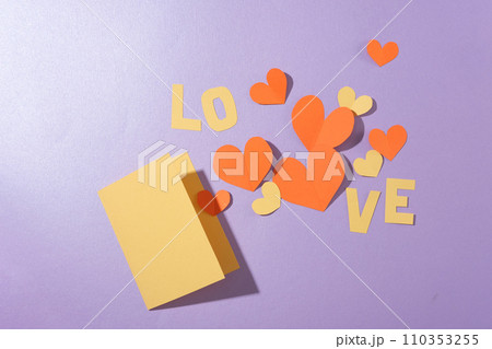 Flat lay of a card, the word LOVE and paper hearts arranged on a pastel purple background. Empty space for anniversary text design. View from above. Flat lay of a card, the word LOVE and paper hearts arranged on a pastel purple background. Empty space for anniversary text design. View from above. 110353255